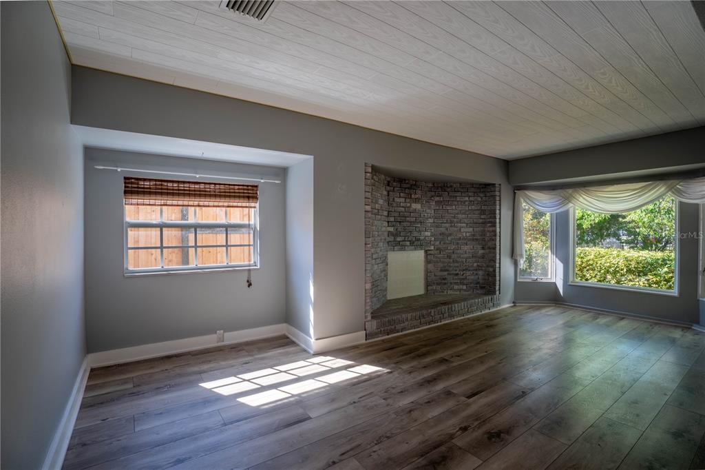 A living room features gray walls, wood-look flooring, a white plank ceiling, and a brick fireplace — 2567 CENTRAL AVENUE, CLEARWATER, FL