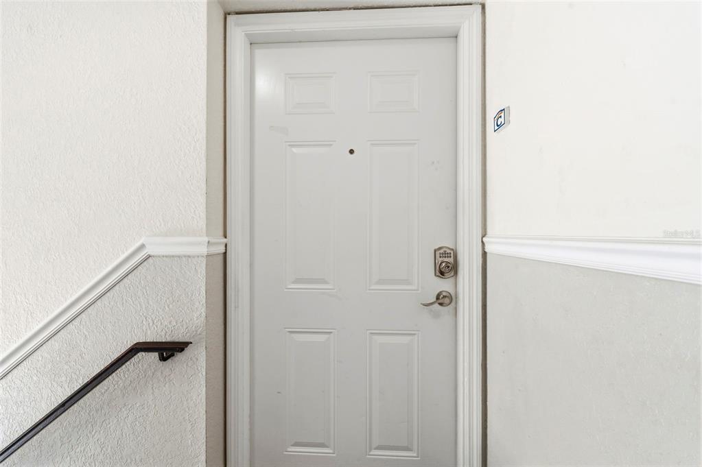 A white six-panel door with a keypad lock is situated in a stairwell — 201 POMPANO DRIVE SE UNIT C furnished, ST PETERSBURG, FL