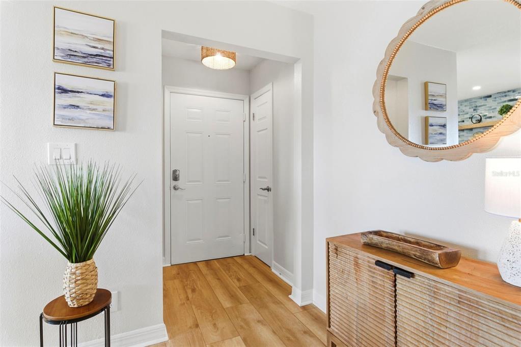 An entryway features light wood flooring, a white front door, and a wooden console table — 201 POMPANO DRIVE SE UNIT C furnished, ST PETERSBURG, FL