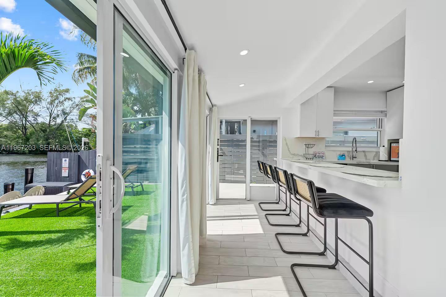 A sunroom with a bar counter, stools, and sliding glass doors opening to a waterfront patio — 1469 NW 10th St, Dania Beach FL 33004, DANIA BEACH, FL