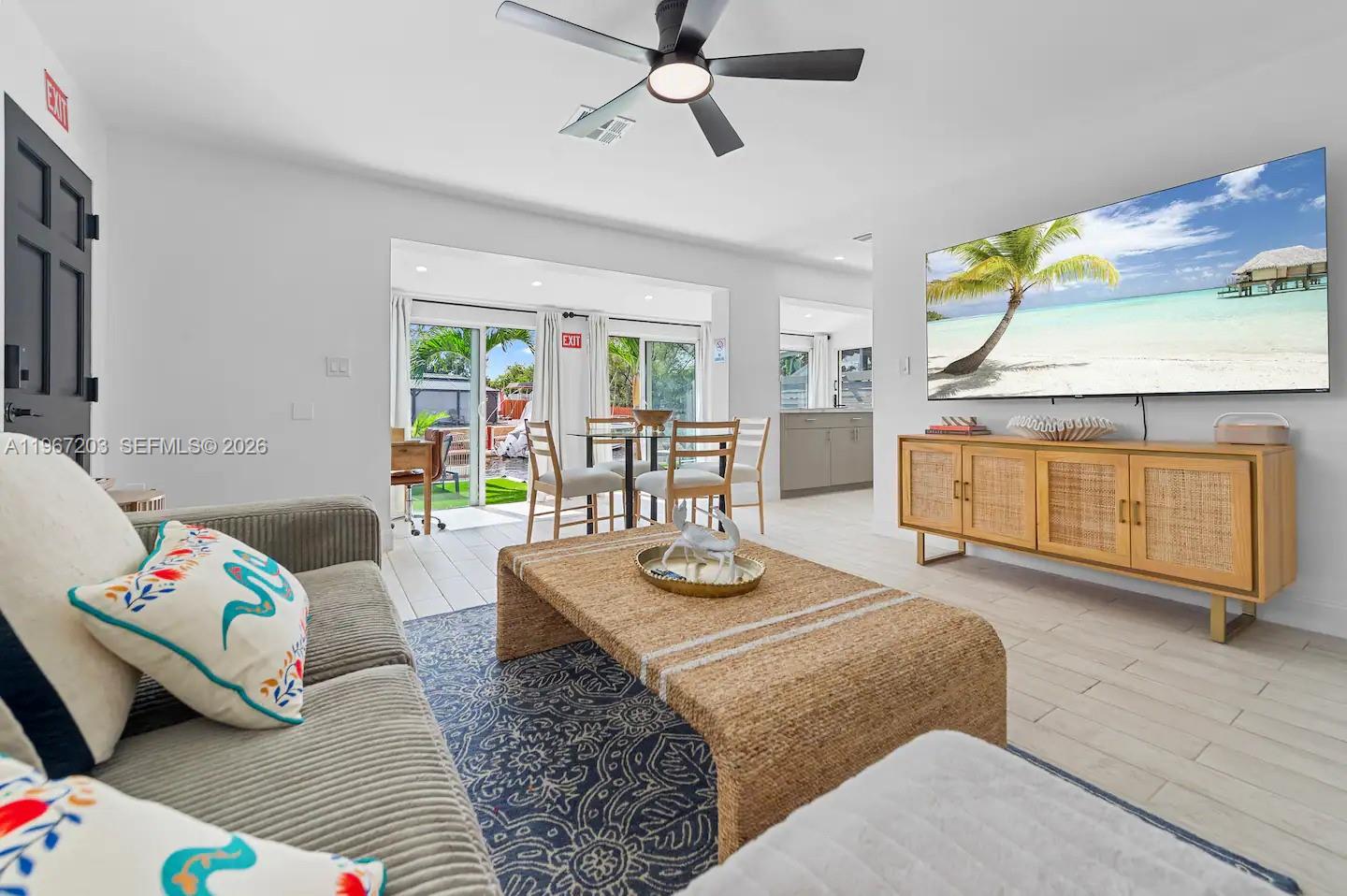 A living room features a television, a rattan coffee table, and sliding glass doors — 1469 NW 10th St, Dania Beach FL 33004, DANIA BEACH, FL
