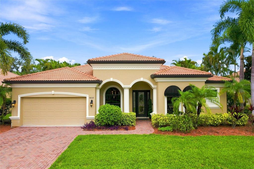 A single-story house with a tan stucco exterior, tile roof, and a brick driveway — 8059 36TH STREET CIRCLE E, SARASOTA, FL