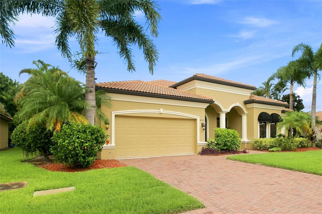 A tan, single-story stucco house with a tile roof, two-car garage, and palm trees — 8059 36TH STREET CIRCLE E, SARASOTA, FL