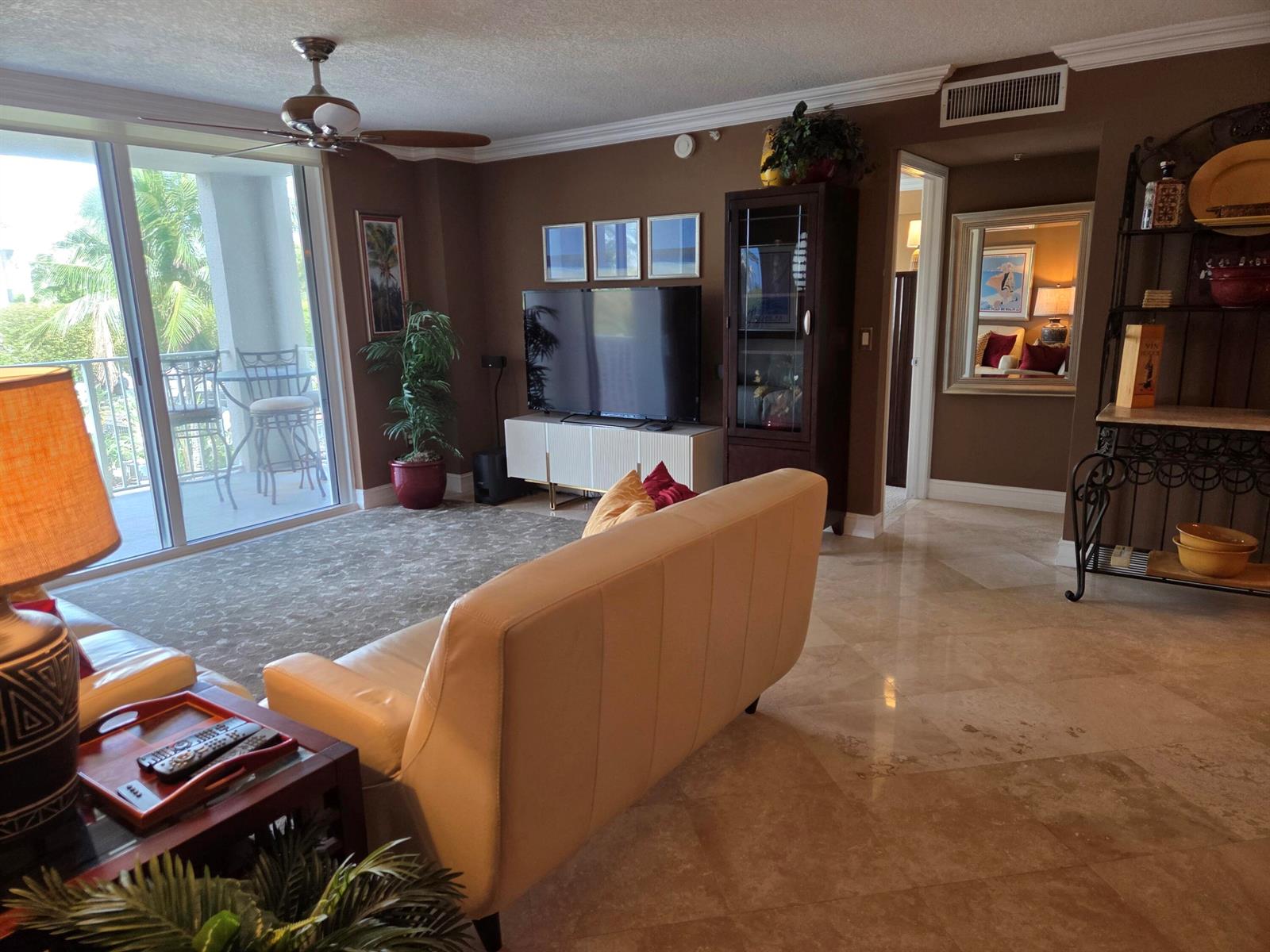 A living room features a white sofa, a television console, and tile flooring near a balcony — 3606 S Ocean Boulevard # 303, Highland Beach FL 33487, HIGHLAND BEACH, FL