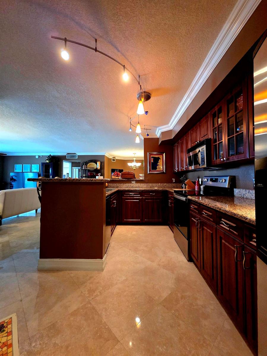 A kitchen with dark wood cabinets, granite countertops, and a curved track lighting fixture — 3606 S Ocean Boulevard # 303, Highland Beach FL 33487, HIGHLAND BEACH, FL