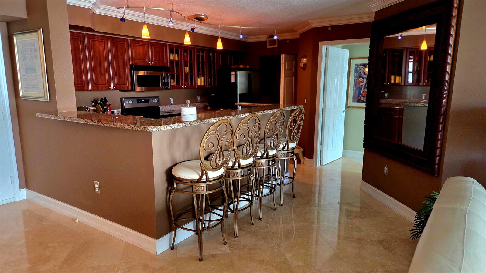A kitchen with dark wood cabinets, granite countertops, and four decorative metal bar stools — 3606 S Ocean Boulevard # 303, Highland Beach FL 33487, HIGHLAND BEACH, FL