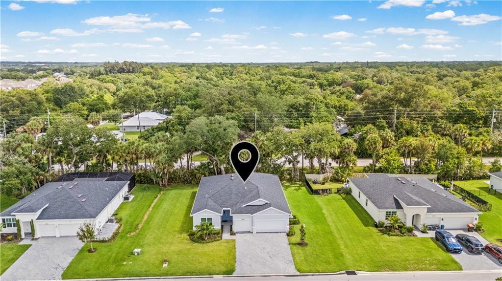 An aerial view shows three suburban houses with gray roofs and green lawns — VERO BEACH, FL
