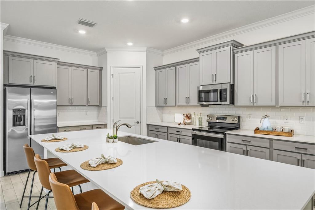 A modern kitchen features gray cabinets, a large white island, and stainless steel appliances — VERO BEACH, FL