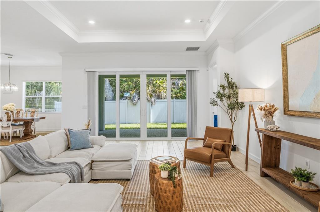 A bright living room features a white sectional sofa, leather armchair, and sliding glass doors — VERO BEACH, FL