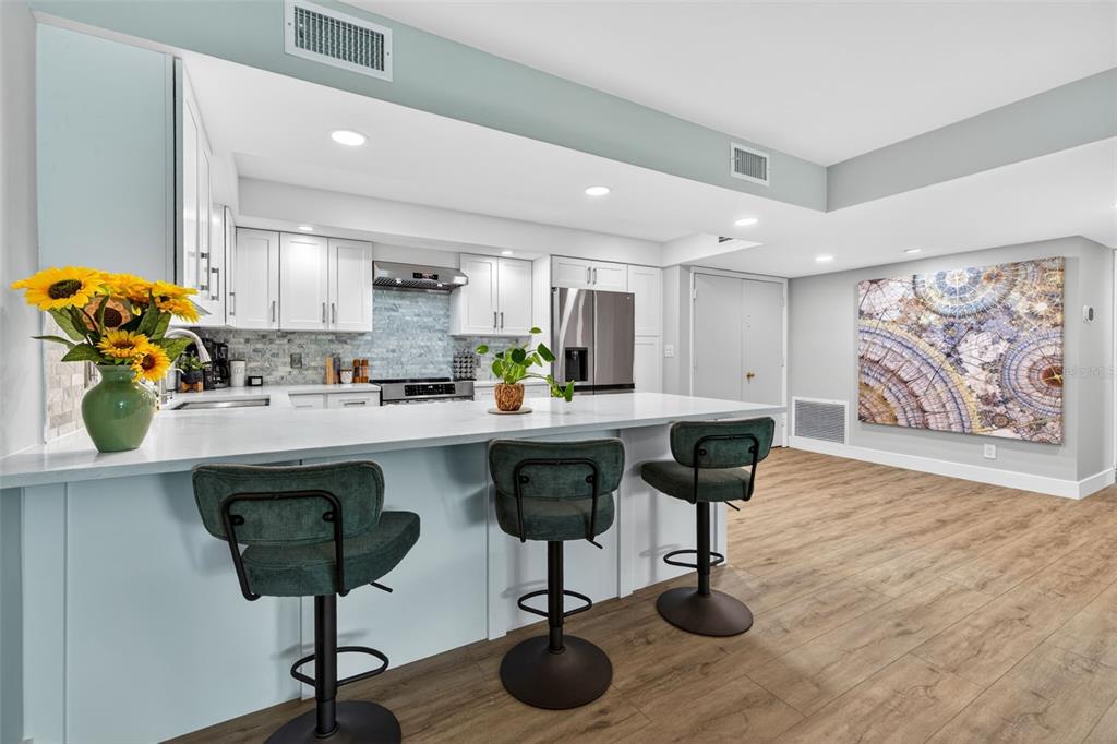 A modern kitchen features white cabinets, a quartz island with three stools, and wood flooring — 100 OAKMONT LANE UNIT 107 & 108, BELLEAIR, FL