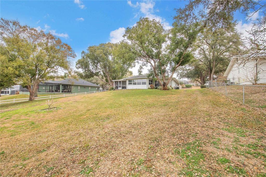 A grassy backyard features mature trees, a white fence, and a single-story house — 194 S LAKE MARIAM DRIVE, WINTER HAVEN, FL