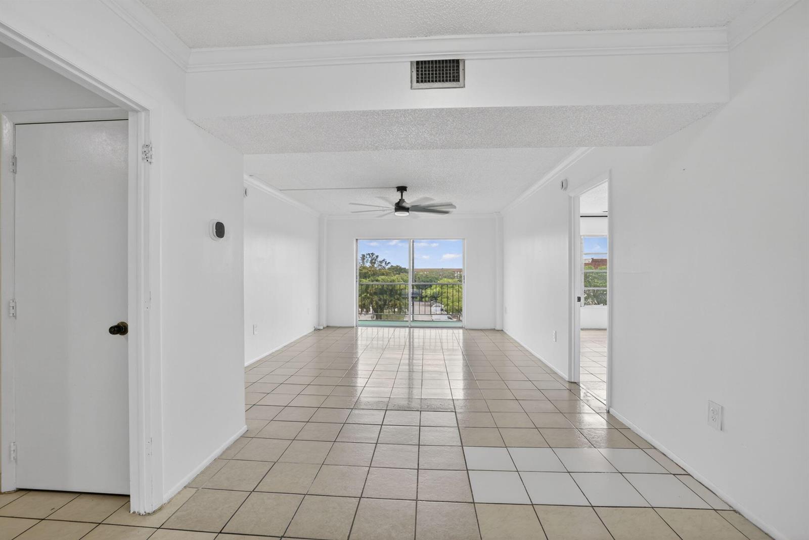 An empty living room with white walls, tile flooring, a ceiling fan, and sliding doors — 4174 Inverrary Drive # 513, Lauderhill FL 33319, LAUDERHILL, FL