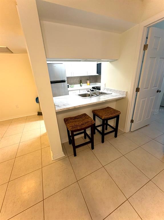A kitchen features a breakfast bar with two stools, white cabinets, and tile flooring — 5132 AMULET DRIVE UNIT 107, NEW PORT RICHEY, FL