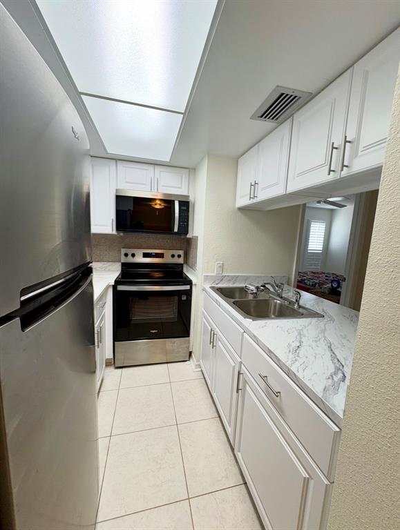 A galley kitchen features white cabinets, stainless steel appliances, and marble-look countertops — 5132 AMULET DRIVE UNIT 107, NEW PORT RICHEY, FL