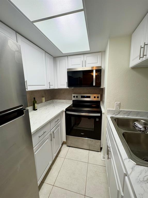 A galley kitchen features white cabinets, stainless steel appliances, and marble-look countertops — 5132 AMULET DRIVE UNIT 107, NEW PORT RICHEY, FL