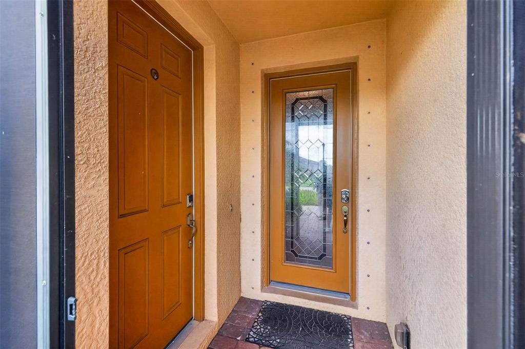 An entryway features a solid wood door and a glass-paneled door with a brick floor — 20630 GRANLAGO DRIVE, VENICE, FL