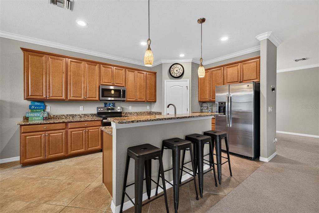 A kitchen with wood cabinets, granite countertops, stainless steel appliances, and a breakfast bar with stools — 20630 GRANLAGO DRIVE, VENICE, FL