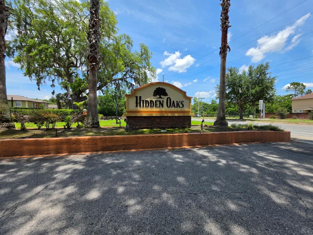 A stone monument sign for Hidden Oaks stands between two palm trees under a blue sky — 7450 WYNNEWOOD SQUARE UNIT 189, WINTER PARK, FL