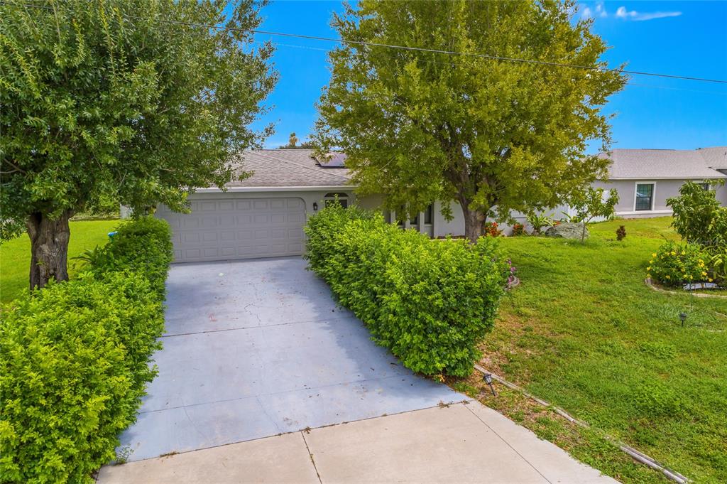 A single-story house with a gray garage door, a concrete driveway, and surrounding green landscaping — 1121 NE 11TH TERRACE, CAPE CORAL, FL