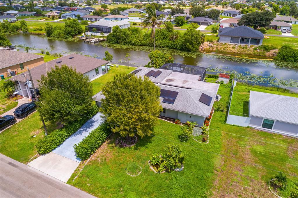 An aerial view shows a residential house with solar panels and a pool cage by water — 1121 NE 11TH TERRACE, CAPE CORAL, FL