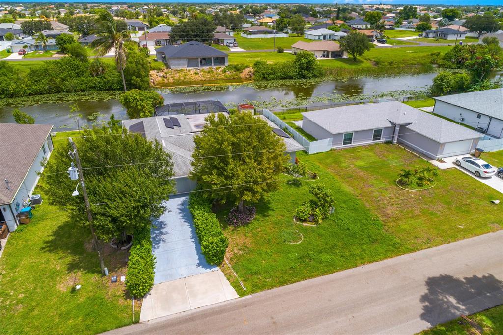 An aerial view shows a house with a driveway, large trees, and a backyard canal — 1121 NE 11TH TERRACE, CAPE CORAL, FL