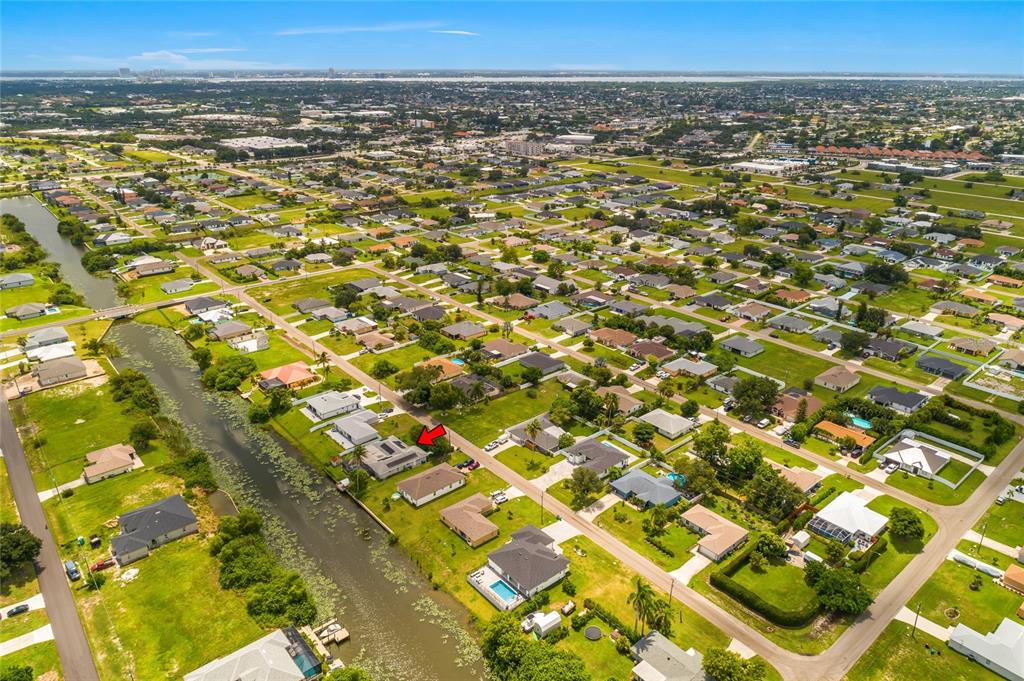 An aerial view shows a residential neighborhood with a canal and a red arrow marker — 1121 NE 11TH TERRACE, CAPE CORAL, FL