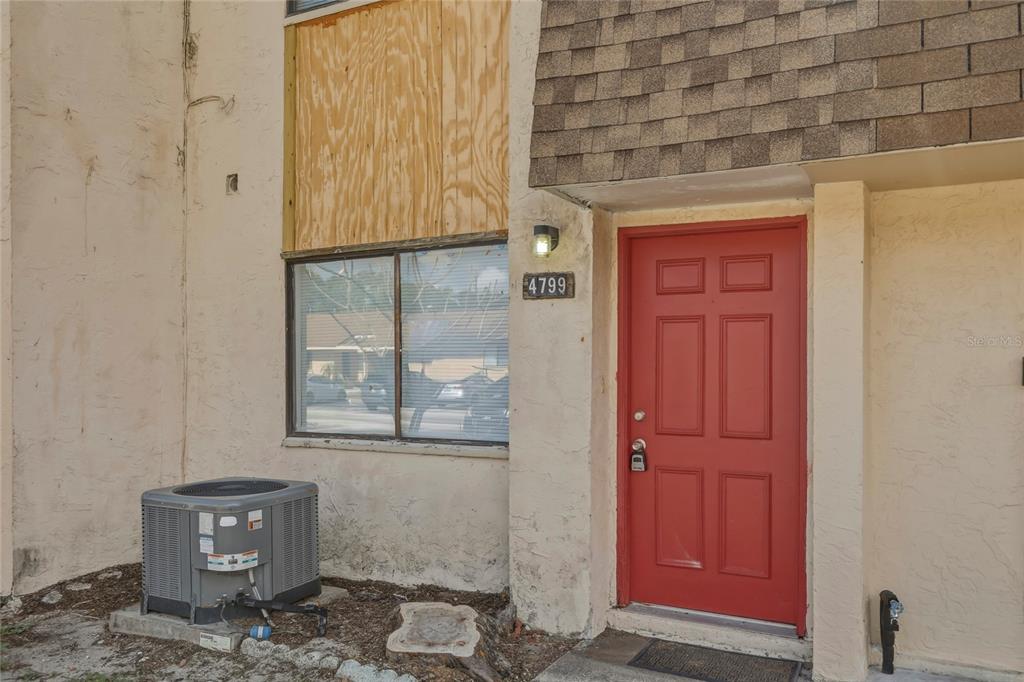 A red front door and a window covered with plywood on a stucco exterior — 4799 SISSON ROAD, TITUSVILLE, FL