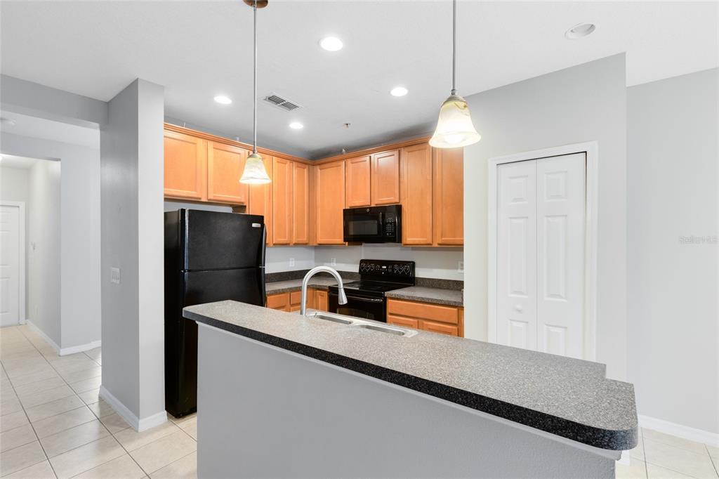 A kitchen features light wood cabinets, black appliances, a breakfast bar, and tile flooring — 2064 CYPRESS BAY BOULEVARD, KISSIMMEE, FL
