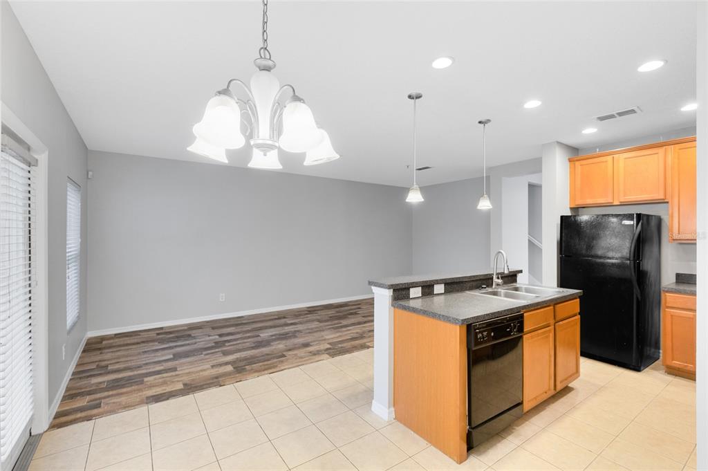 A kitchen with wood cabinets and a black refrigerator opens to a dining area — 2064 CYPRESS BAY BOULEVARD, KISSIMMEE, FL