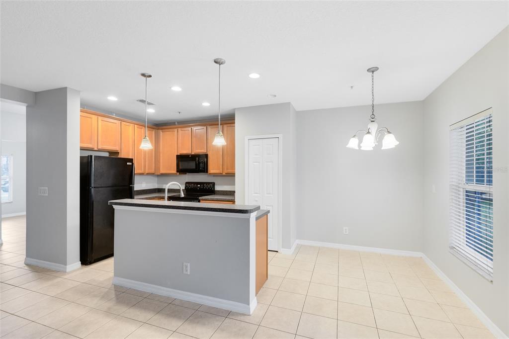 A kitchen with light wood cabinets, black appliances, and a breakfast bar overlooks a dining area — 2064 CYPRESS BAY BOULEVARD, KISSIMMEE, FL