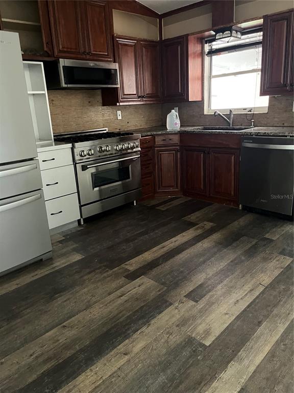 A kitchen features dark wood cabinets, stainless steel appliances, and wood-look plank flooring — 1202 INGRAM STREET, KISSIMMEE, FL