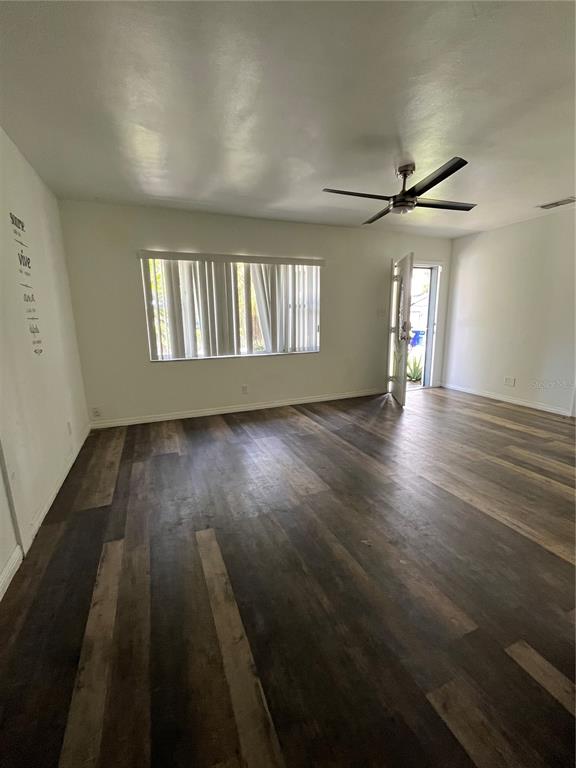 An empty room features dark wood-look flooring, a ceiling fan, and a window with blinds — 1202 INGRAM STREET, KISSIMMEE, FL