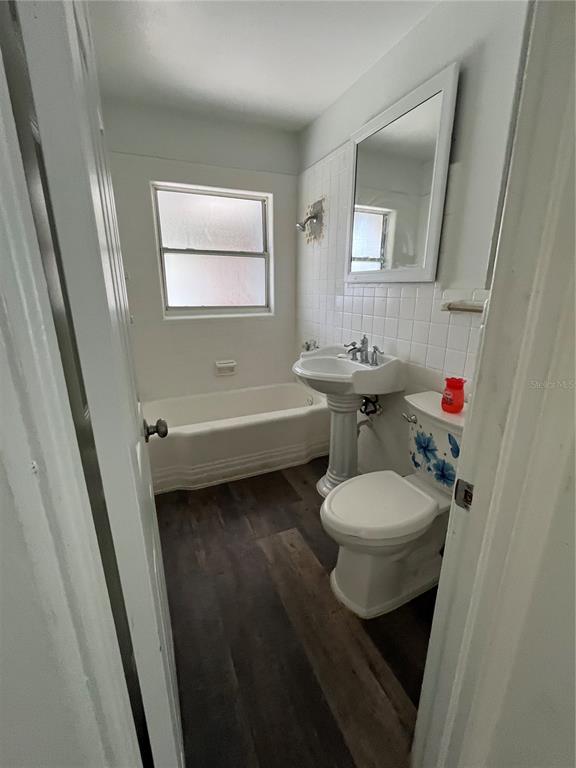 A bathroom features a pedestal sink, a toilet, a bathtub, and dark wood-look flooring — 1202 INGRAM STREET, KISSIMMEE, FL