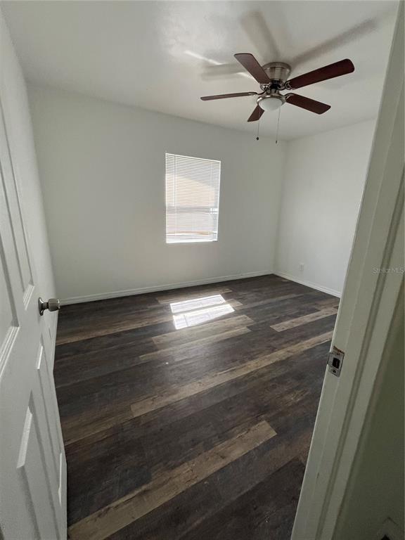 An empty bedroom features white walls, a ceiling fan, and dark wood-look plank flooring — 1202 INGRAM STREET, KISSIMMEE, FL