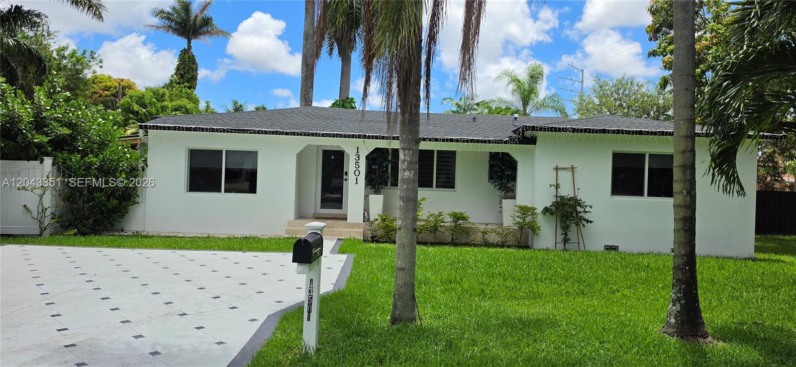 A white single-story house features a dark shingled roof, a front porch, and a driveway — 13501 NE Miami Ct, Miami FL 33161, MIAMI, FL