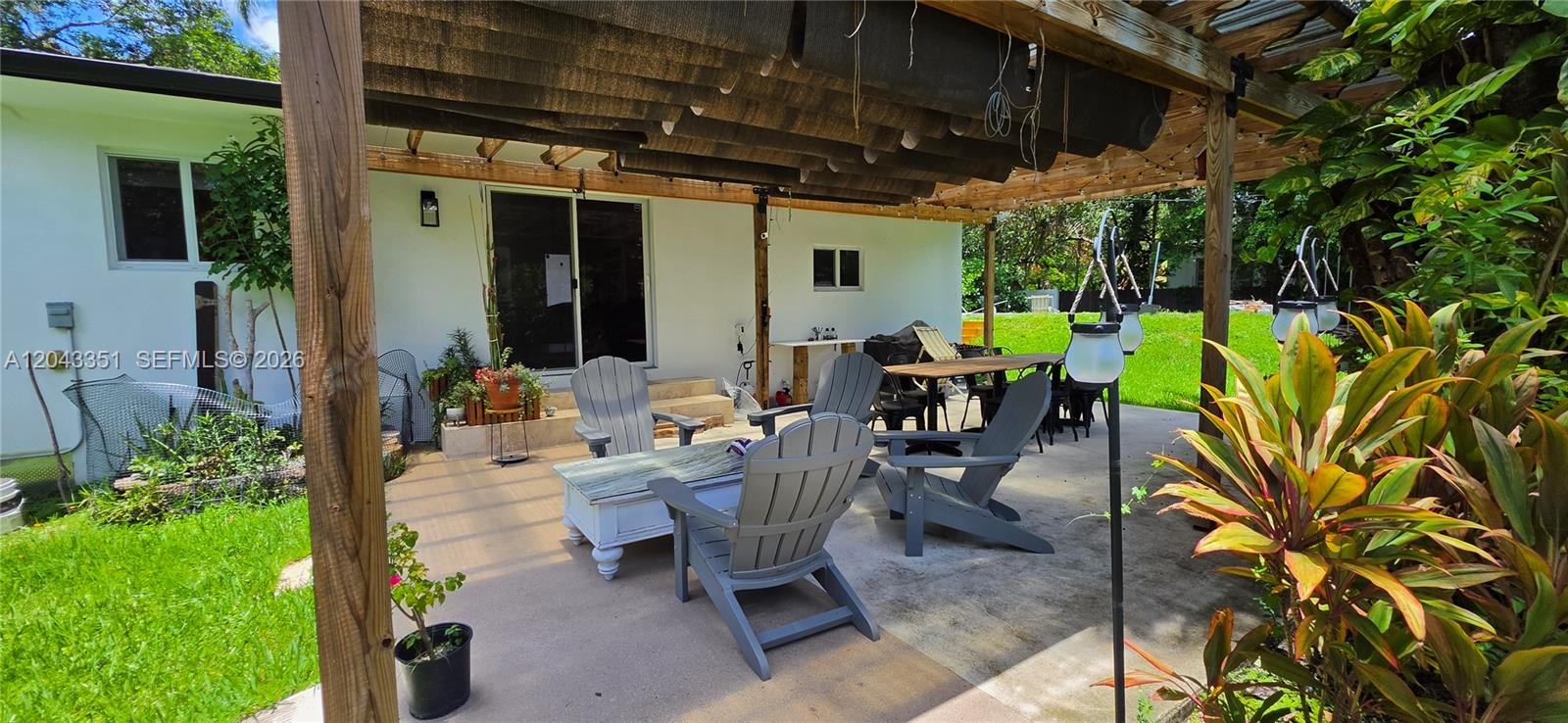 A covered patio features a wooden pergola, gray Adirondack chairs, and a dining table — 13501 NE Miami Ct, Miami FL 33161, MIAMI, FL