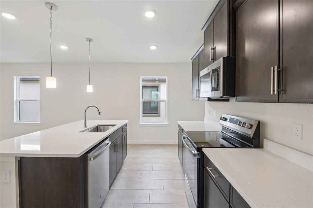 A modern kitchen features dark wood cabinets, white countertops, stainless steel appliances, and tile flooring — 3346 CUP DRIVE, LAKELAND, FL
