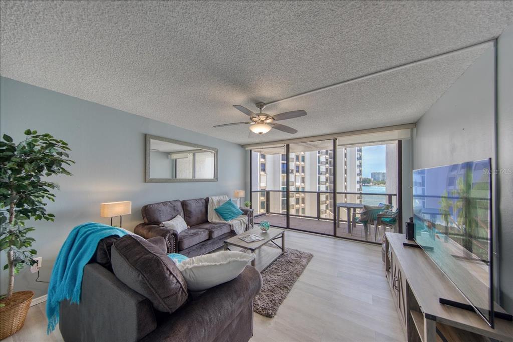 A living room with gray sofas, a ceiling fan, and a balcony overlooking the water — 440 S GULFVIEW BOULEVARD UNIT 701, CLEARWATER BEACH, FL