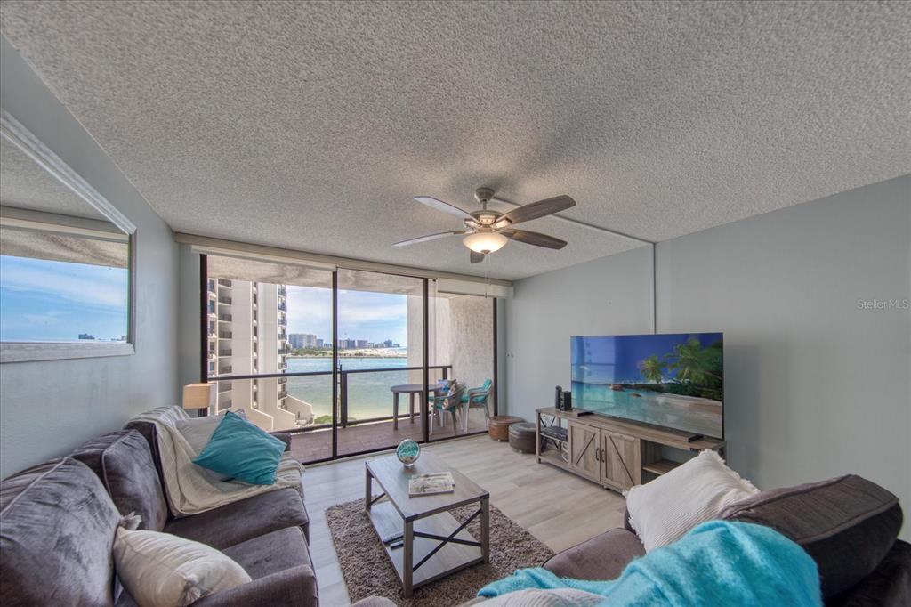 A living room with a ceiling fan, gray sofas, and a balcony overlooking the ocean — 440 S GULFVIEW BOULEVARD UNIT 701, CLEARWATER BEACH, FL