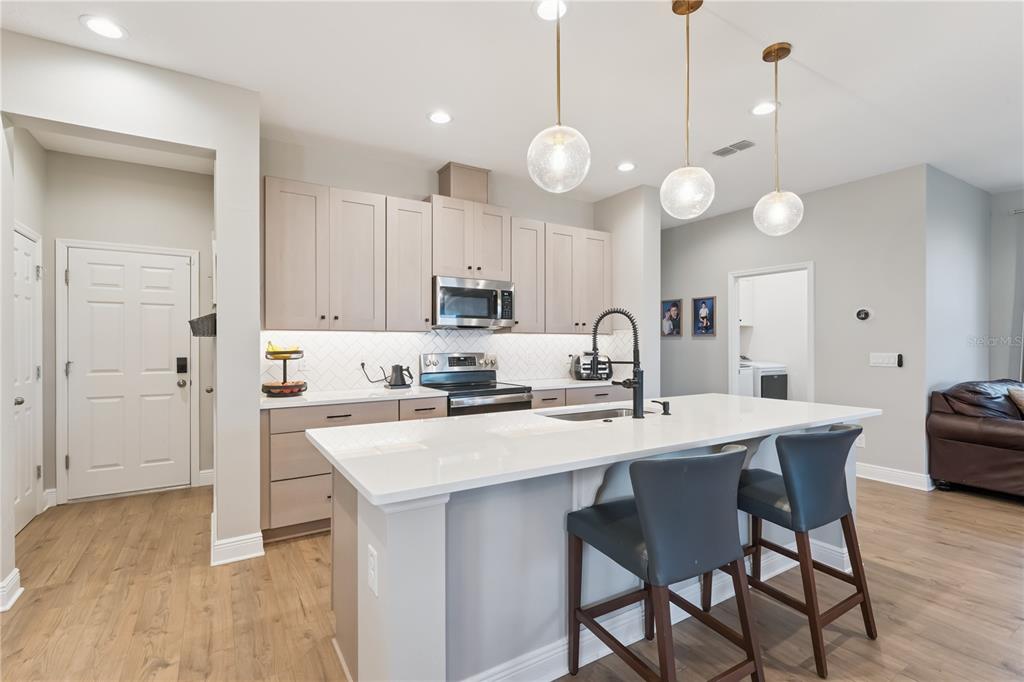 A modern kitchen features light wood cabinets, white countertops, a central island, and pendant lighting — 14434 CRESTAVISTA AVENUE, CLERMONT, FL