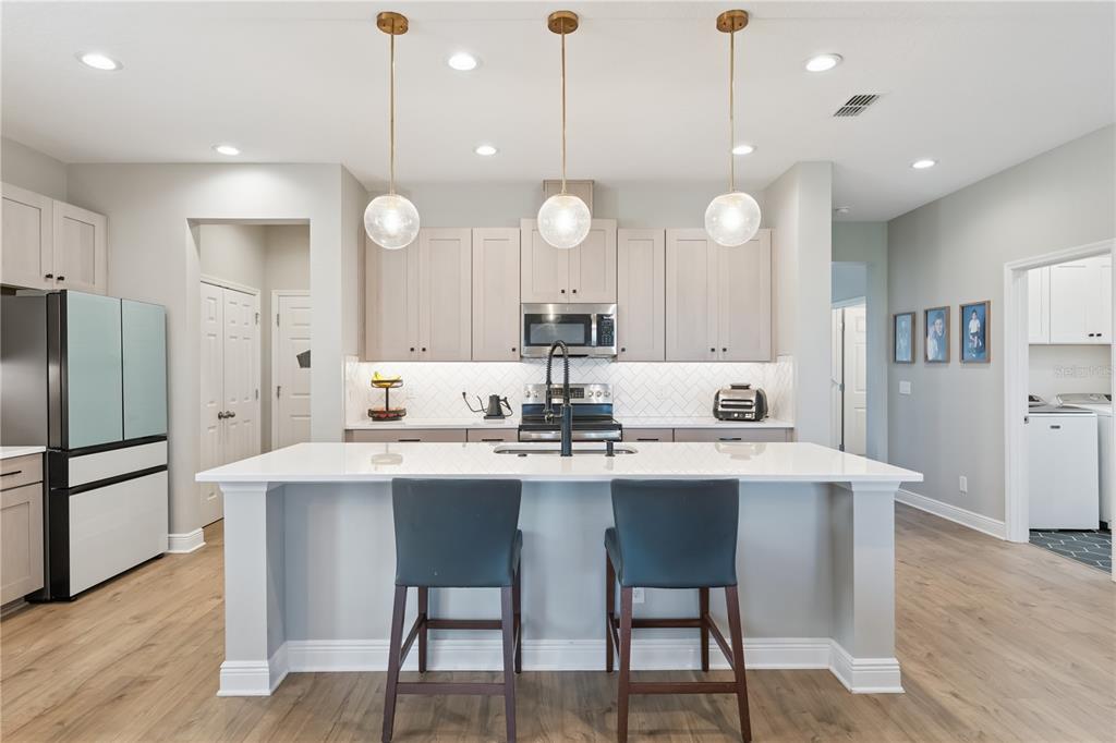 A modern kitchen features light wood cabinets, a white island with stools, and pendant lighting — 14434 CRESTAVISTA AVENUE, CLERMONT, FL