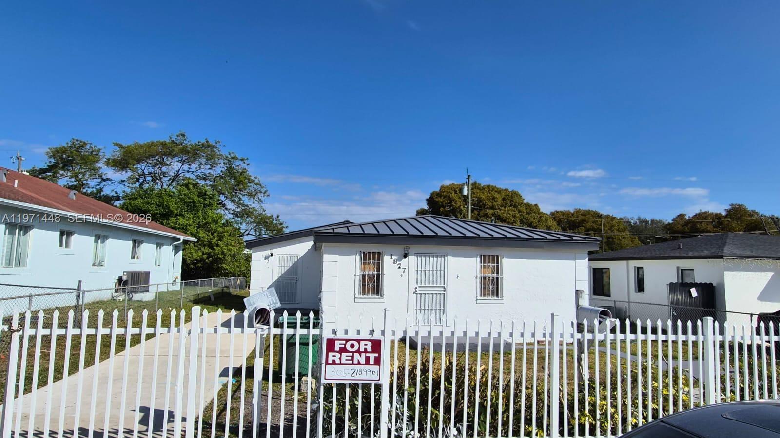 A white single-story house with a metal roof stands behind a white metal fence — 1827 NW 74th Ter, Miami FL 33147, MIAMI, FL