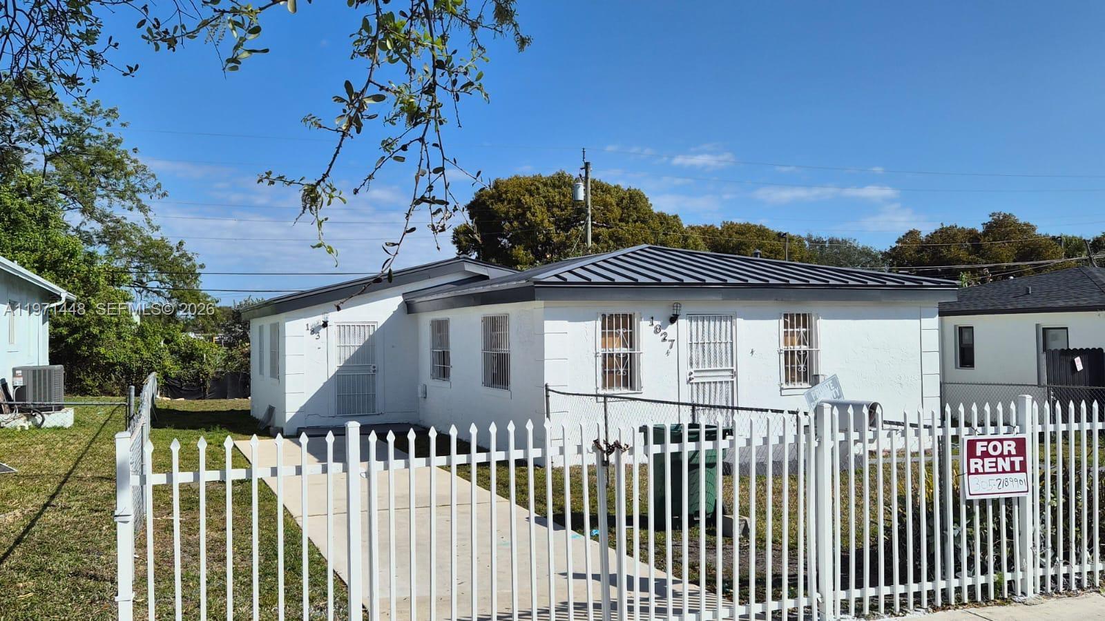 A white single-story house with a metal roof sits behind a white picket fence — 1827 NW 74th Ter, Miami FL 33147, MIAMI, FL
