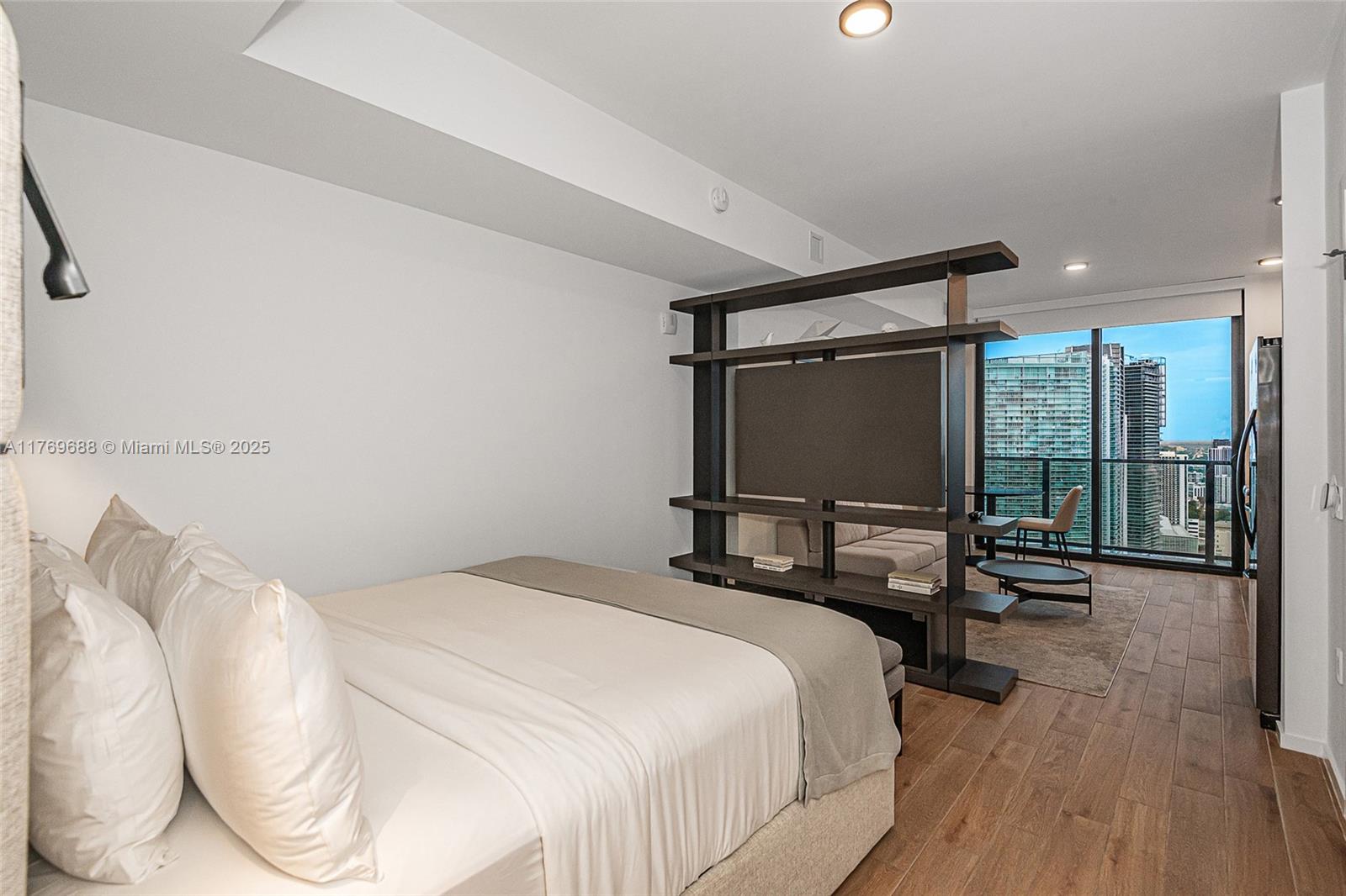 A bedroom with a wooden floor, a central shelving unit, and a view of city skyscrapers — 398 NE 5th St # 4008, Miami FL 33132, MIAMI, FL
