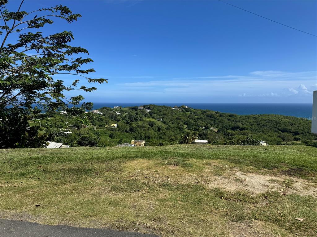 A grassy lot overlooks a lush, hilly landscape with a view of the ocean — EL COCAL BEACH AND COUNTRY CLUB UNIT 1, YABUCOA, PR