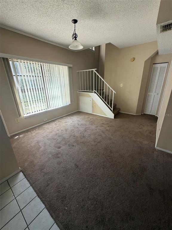 A living room with brown carpet, a large window with blinds, and a staircase — 47 EMERALD BAY DRIVE, OLDSMAR, FL