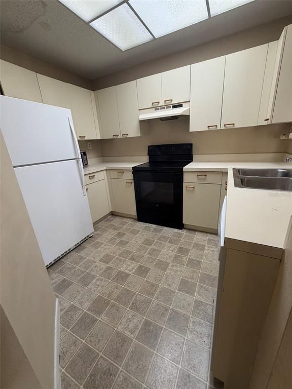 A kitchen features white cabinets, a black stove, a white refrigerator, and checkered flooring — 47 EMERALD BAY DRIVE, OLDSMAR, FL