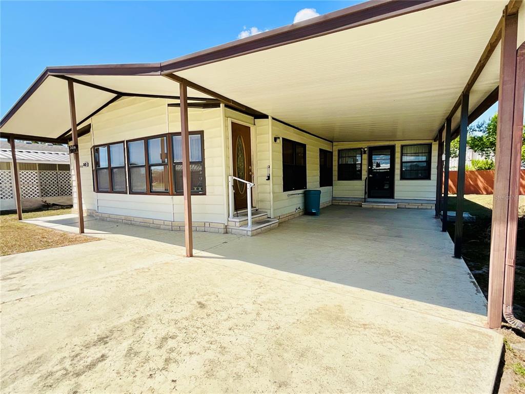 A manufactured home exterior features a large concrete carport and a covered front entryway — 35935 TANDA CIRCLE, ZEPHYRHILLS, FL