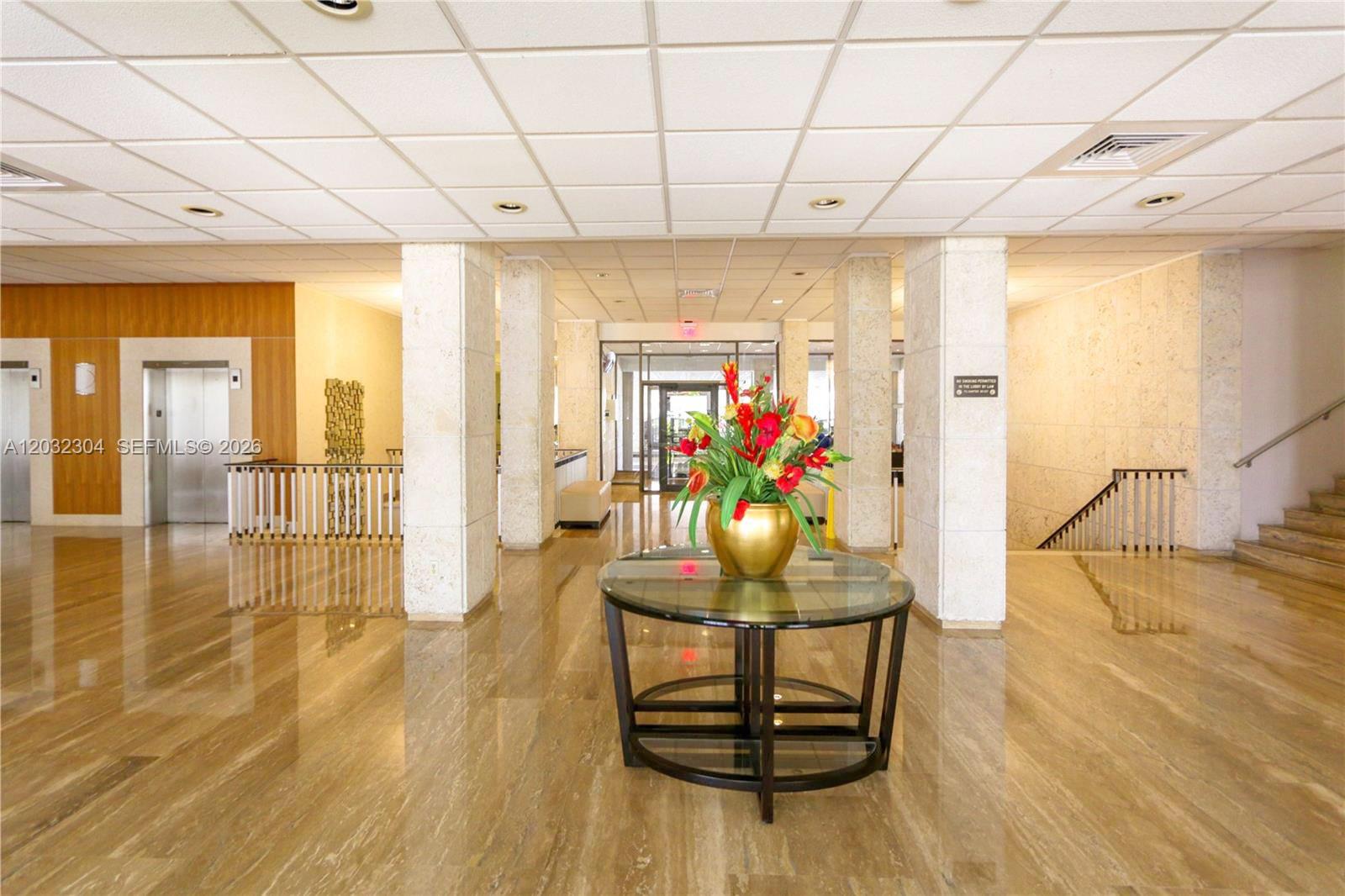 A lobby features a glass-topped table with a floral arrangement, marble floors, and elevators — 1950 S Ocean Dr # 3D, Hallandale Beach FL 33009, HALLANDALE BEACH, FL