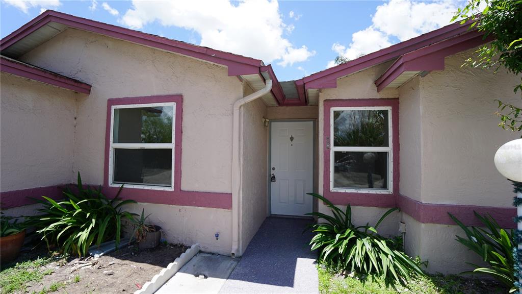 A tan house exterior features a white front door, two windows, and a concrete walkway — 834 ANGELA LANE, KISSIMMEE, FL